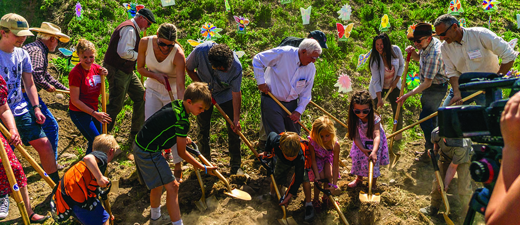 A group of people of all ages breaking ground for the upcoming Rocky Mountain Exploration Center.